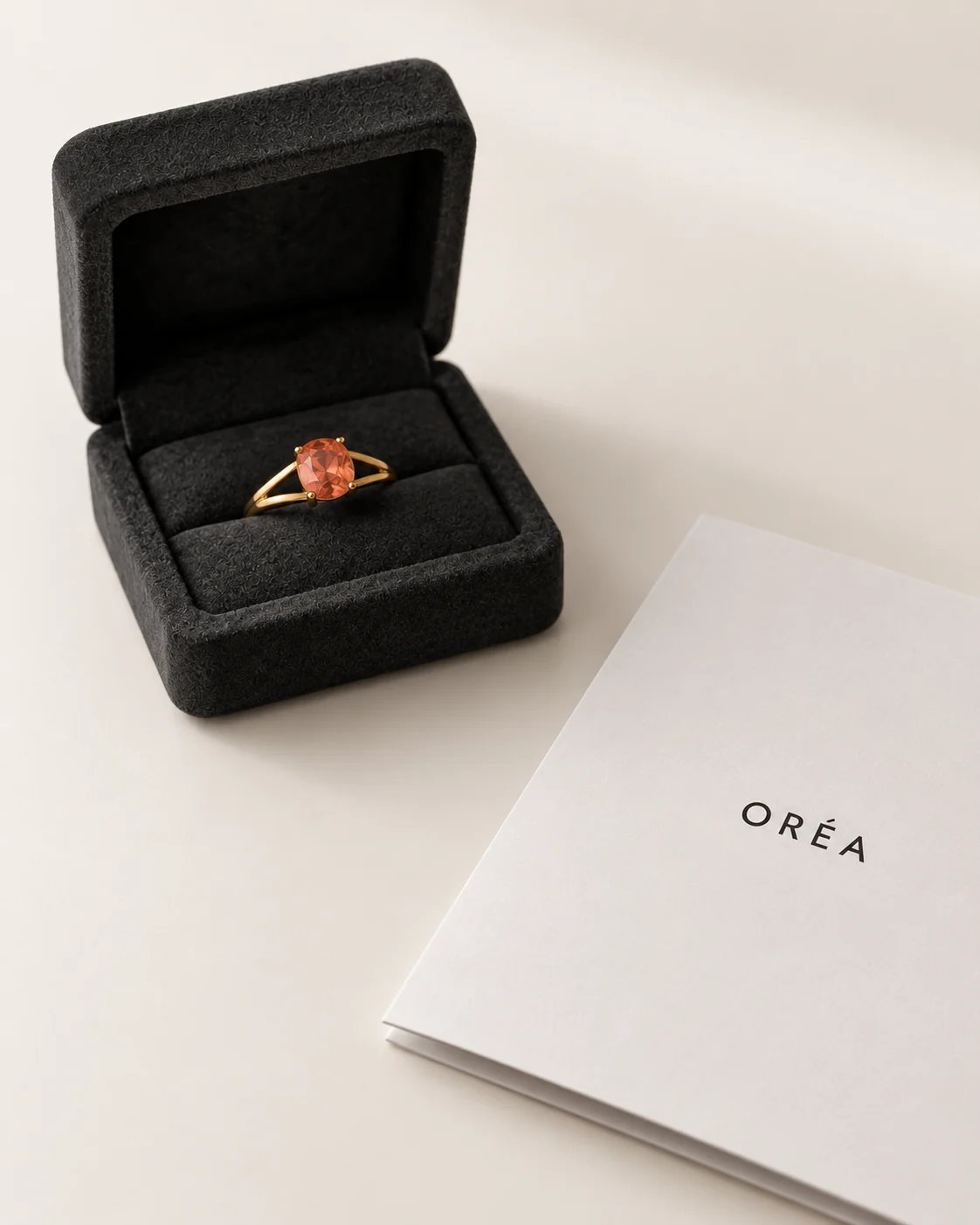 A finished gold ring in an open charcoal suede box, the house's card beside it